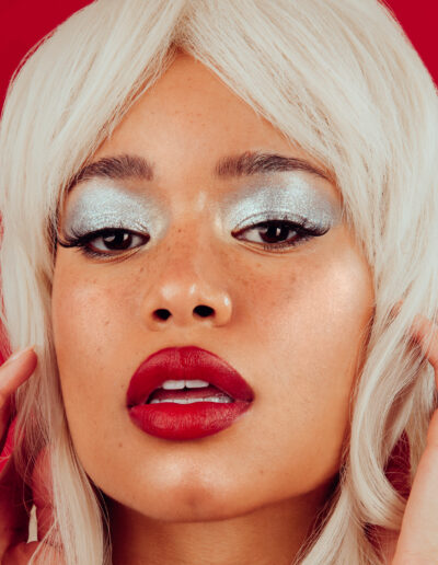 Model Cyan Cosby Poses in a Closeup Photo in a Blonde Wig with Silver Eyeshadow and Red Lipstick